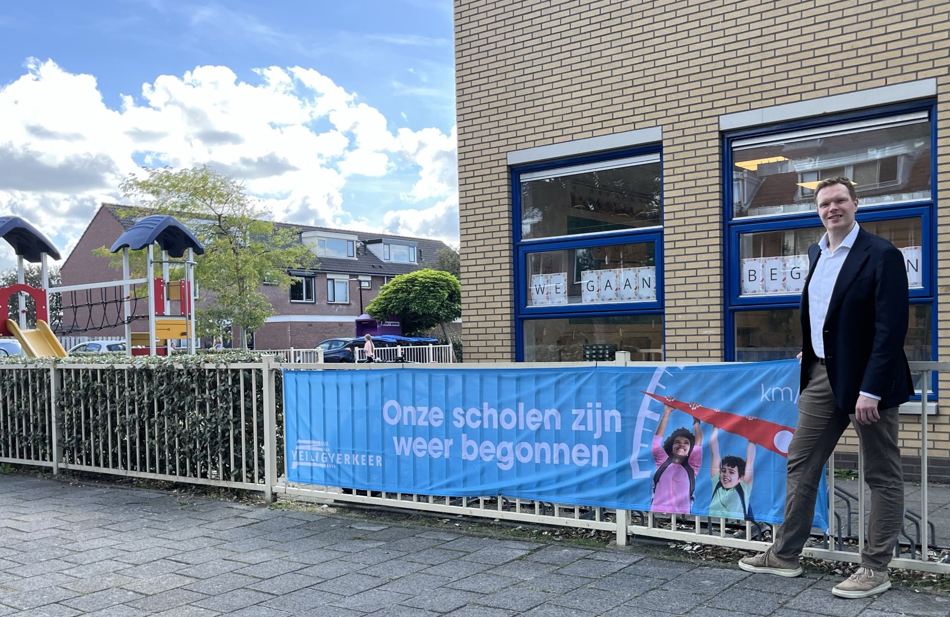 Foto van wethouder Jordy de Mooij voor school met spandoek