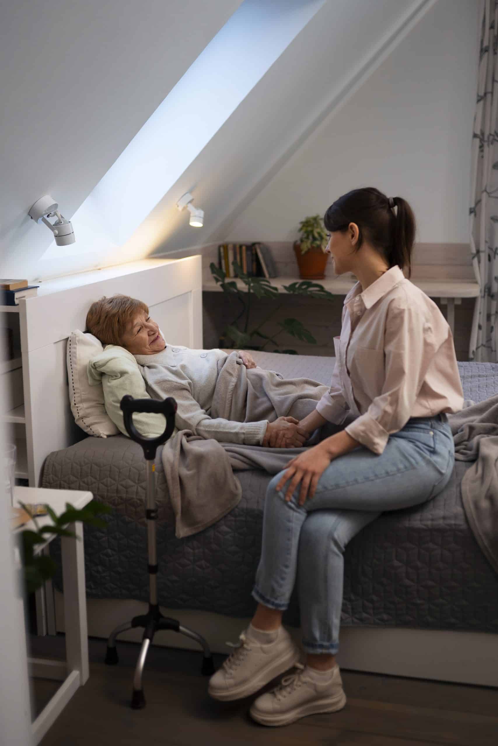een oudere vrouw ligt in bed en wordt verzorgd door een jonge vrouw