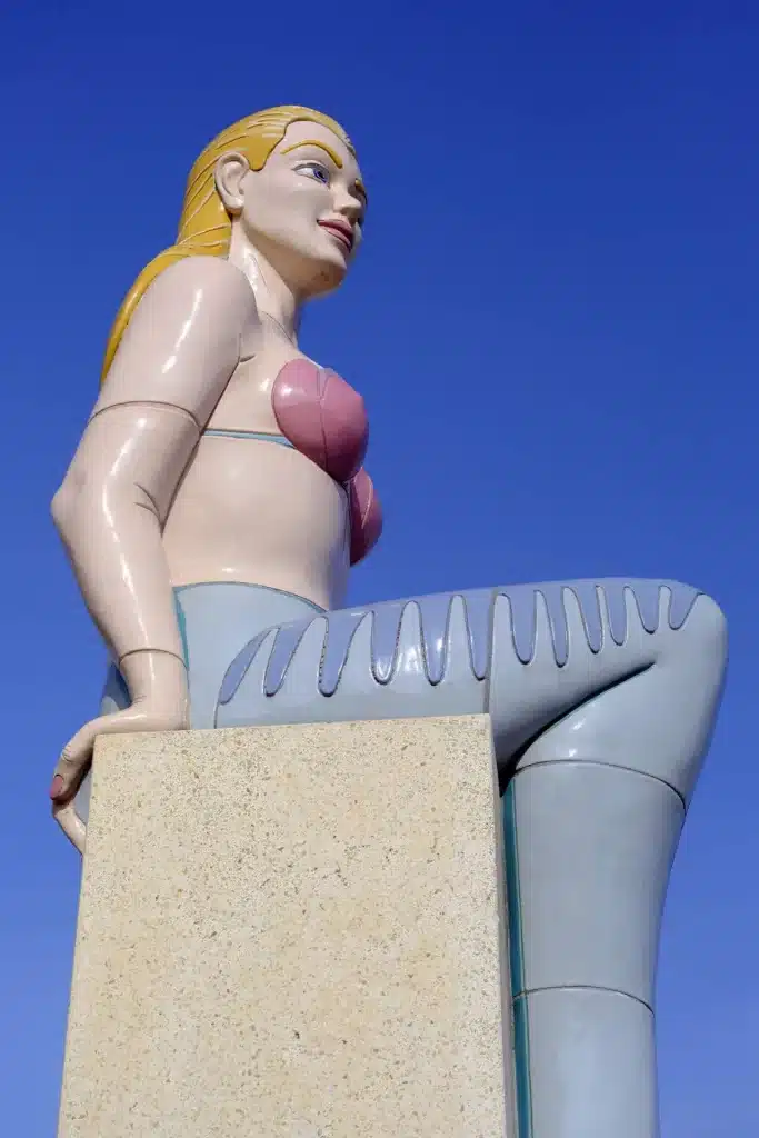 Beeld van een zeemeermin zittend op een steen.