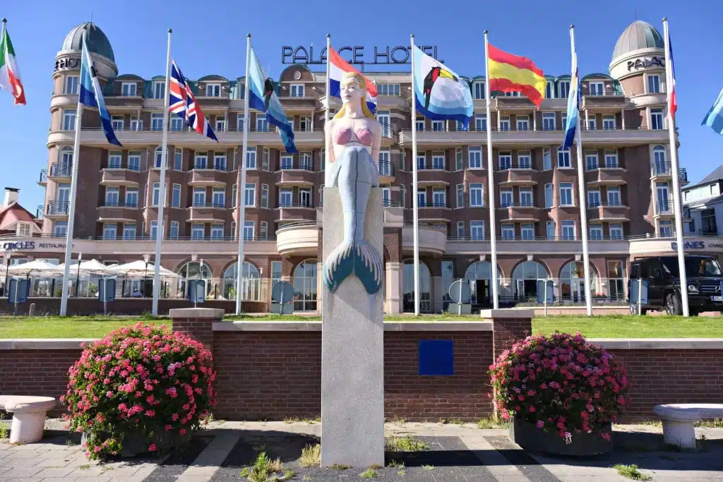 Beeld van een zeemeermin met op de achtergrond een hotel.