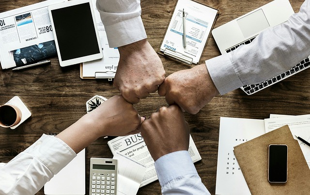 Afbeelding van vuisten tegen elkaar in een cirkel met werk spullen op de tafel eronder liggen. 