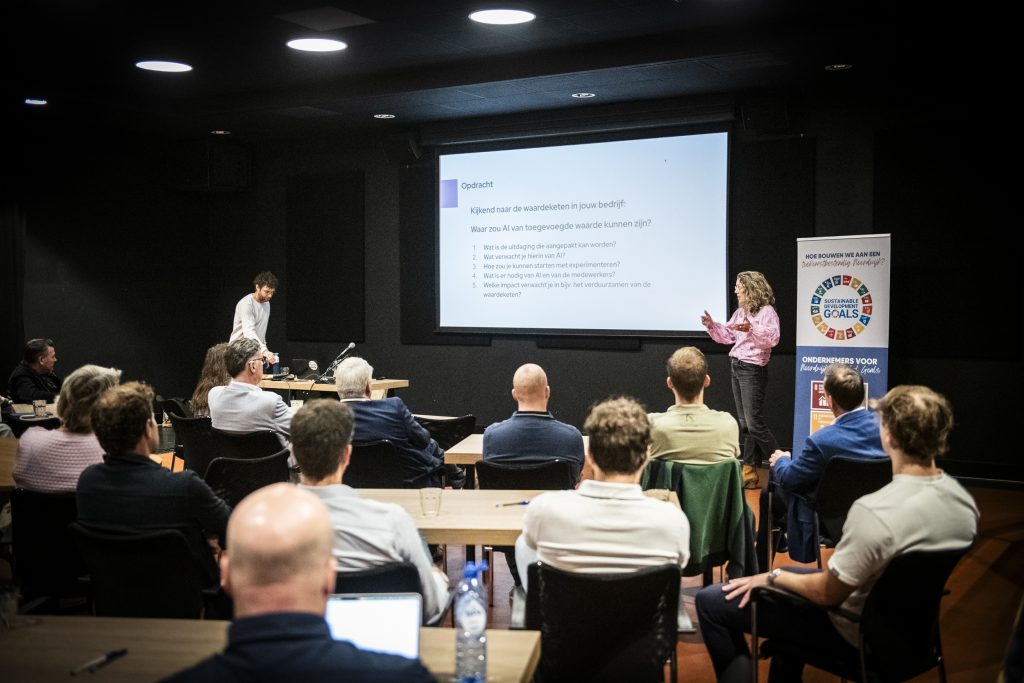 Spreker naast beeldscherm voor groep deelnemers.