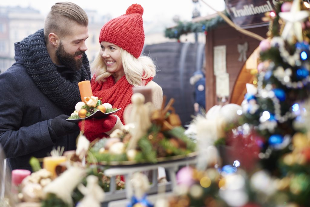 Man en vrouw voor marktkraam die kerststukje vasthouden.