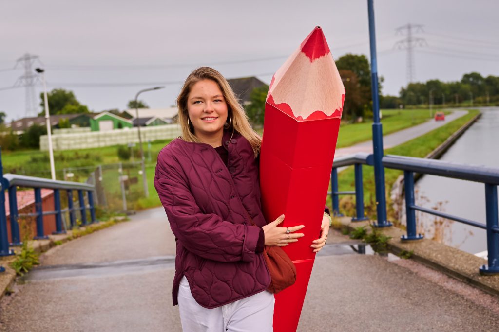 Mevrouw met groot rood potlood op een fietspad.